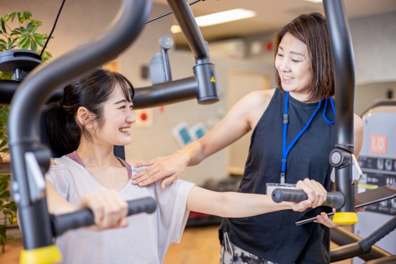 パーソナルジムでトレーナーにサポートしてもらっている女性の写真