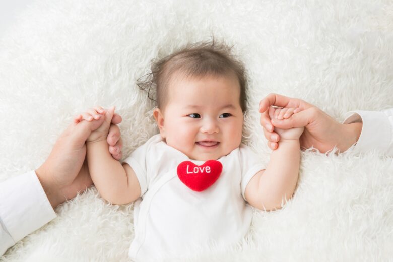 寝転がってママと手を繋いでいる赤ちゃんの写真